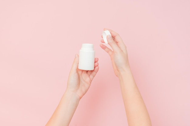 White bottle plastic tube in womans hands on pink background Packaging for pills capsules or supplements Cosmetics