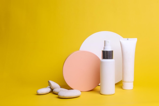 White bottle and tube cosmetic product with round geometric and white stone on yellow background.