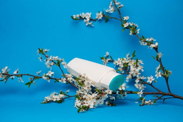 white bottle with cream, shampoo for hair, shower gel, isolated blue background, beauty and youth of the human body, flowering tree