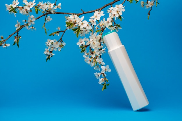 white bottle with cream, shampoo for hair, shower gel, isolated blue background, beauty and youth of the human body, flowering tree