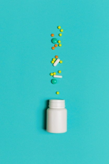 Фото Белая бутылка с различными разноцветными витаминами, таблетками и капсулами на синем фоне