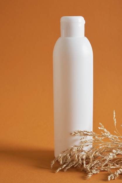 茶色の背景、乾燥ハーブ、自然化粧品の概念にロゴのない白いボトル