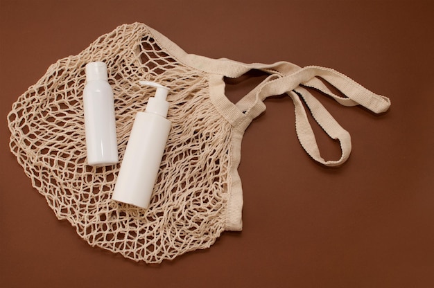 White bottles of cosmetics on a string bag on a brown background with a place for text