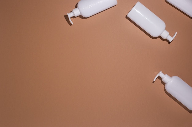 White bottles with a dispenser lie on a brown cardboard background. Top view, flat lay.