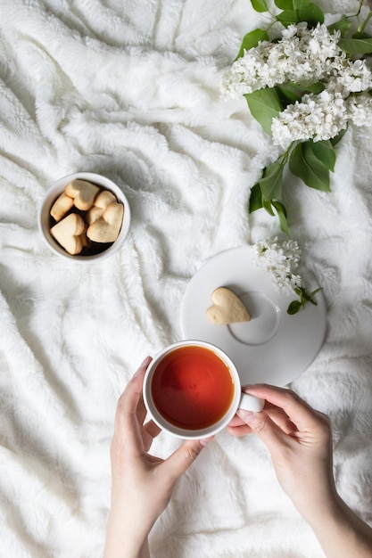 Bouquet bianco di lillà e una tazza di tè fresco profumato in mani femminili sul letto al mattino to