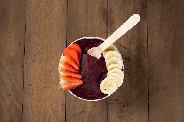 Photo white bowl of brazilian frozen acai berry with banana and strawberry on a wooden desk top view