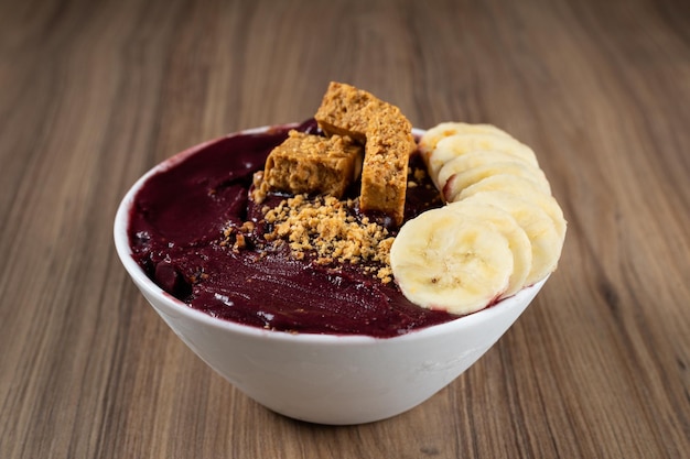 Photo white bowl of brazilian frozen acai berry with pacoca and banana on a wooden desk