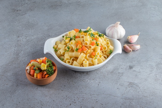 White bowl of delicious pasta with fresh salad on stone surface.