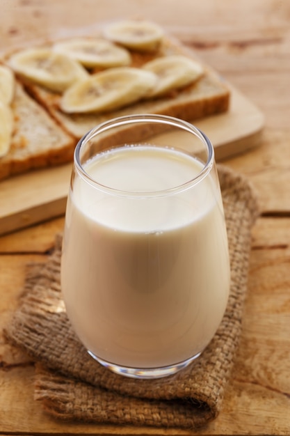 Foto ciotola bianca piena di fiocchi d'avena sani, con banana, latte e pane secco per colazione.