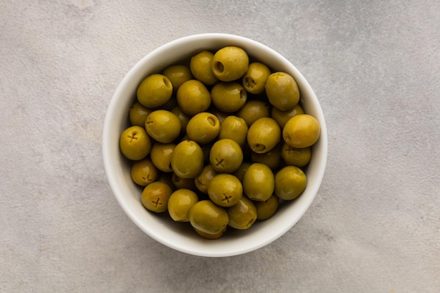 White bowl full of juicy green olives on a light background