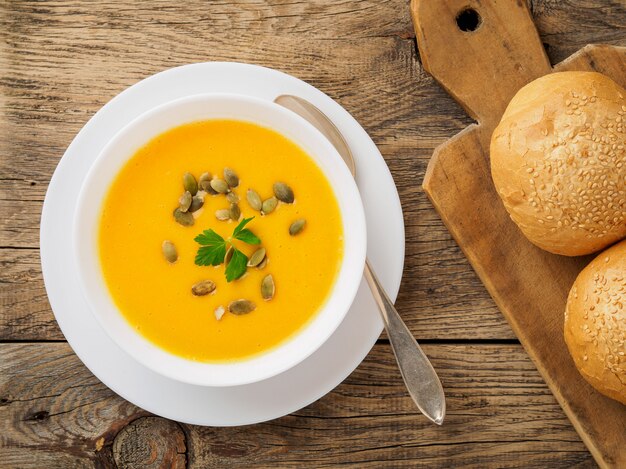 White bowl of pumpkin soup, garnished parsley and sunflower seeds on wooden background