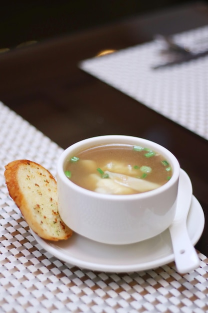 A white bowl of soup with a spoon on the table with a slice of garlic bread