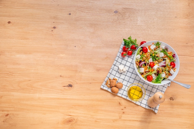 White bowl of vegetarian salad with iceberg lettuce with a mix of healthy ingredients such as walnuts, cherries tomatoes, walnuts, carrots, fresh cheese and corn. top view