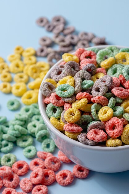 Foto ciotola bianca con cereali colorati a forma di anello e latte su uno sfondo blu