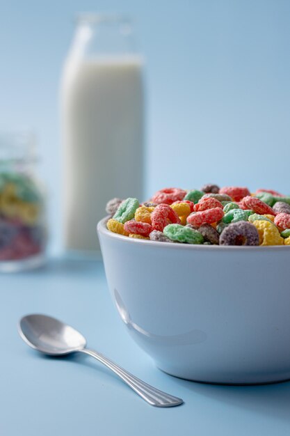 Foto ciotola bianca con cereali colorati a forma di anello e latte su uno sfondo blu