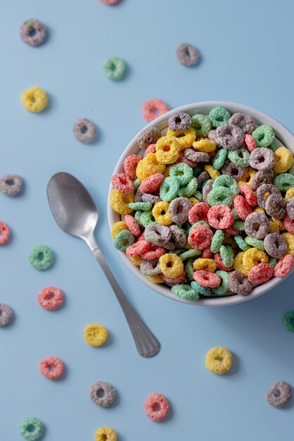 Foto ciotola bianca con cereali colorati a forma di anello e latte su uno sfondo blu