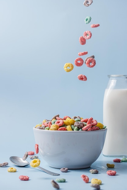 Foto ciotola bianca con cereali colorati a forma di anello e latte cereali e latte versati nella ciotola