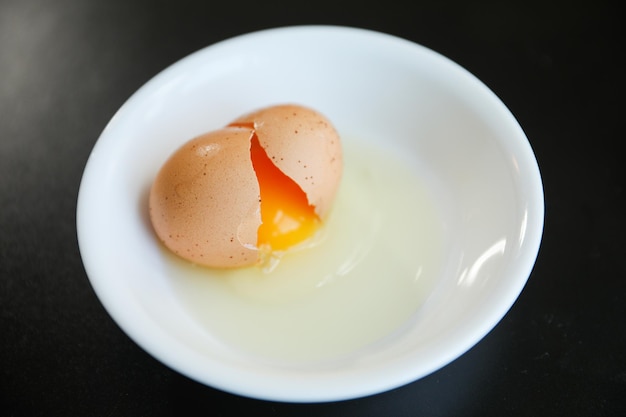 A white bowl with eggs in it and a brown egg in it.