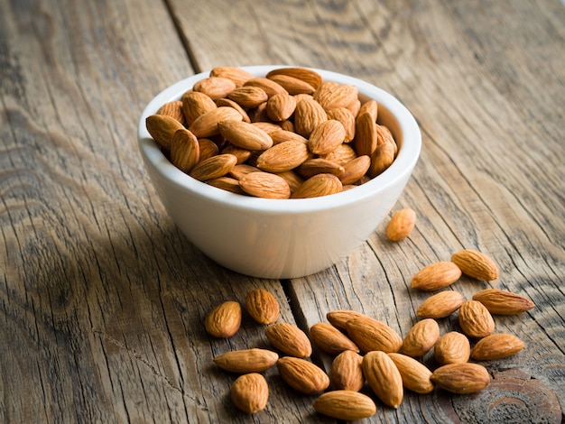 Photo white bowl with a handful of nuts of almonds on a wooden background table