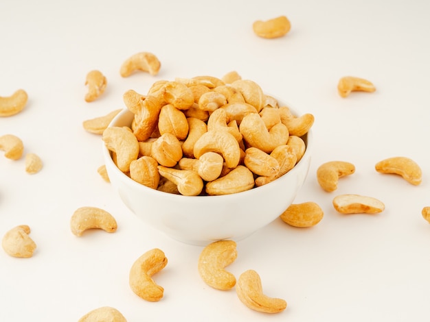 White bowl with a handful of nuts of cashew on white background table