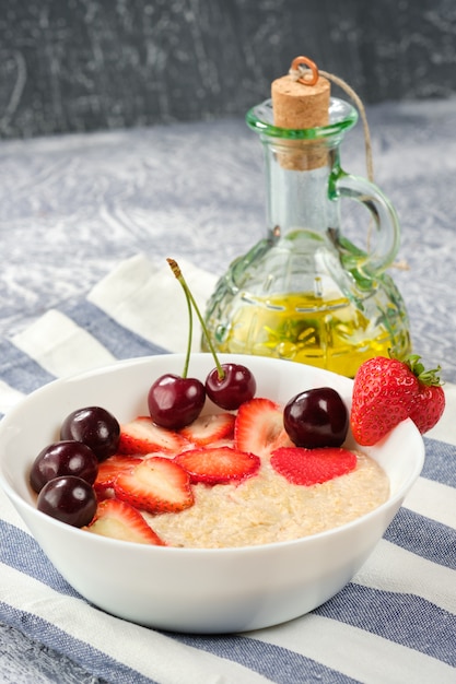 Ciotola bianca con farina d'avena e fragole e ciliegie e olio d'oliva su un tovagliolo a strisce