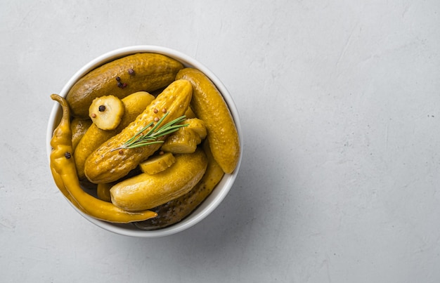 A white bowl with pickled cucumbers with pepper and rosemary on a gray background. Top view, copy space.