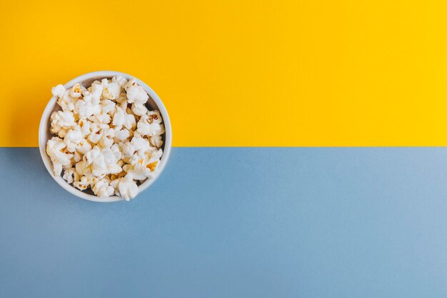 White bowl with popcorn on blue and yellow background. Concept fun plan, watch a movie or a series.