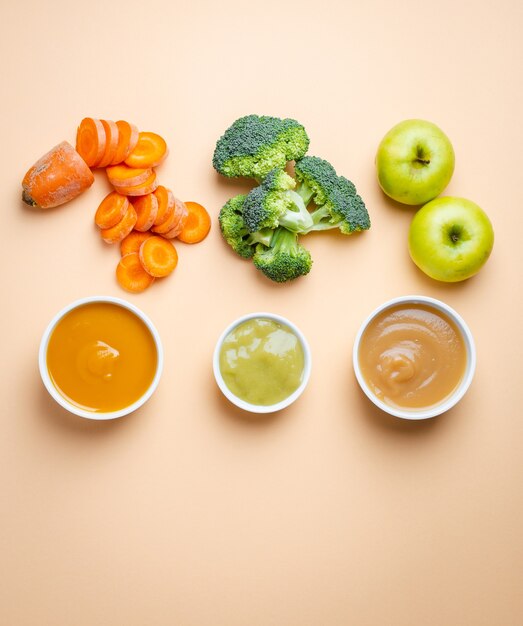 White bowls with healthy natural baby food on pastel background. Purees, made of fresh organic fruit and vegetables, flay lay, top view, concept. Food for kids made from carrot, broccoli, apples