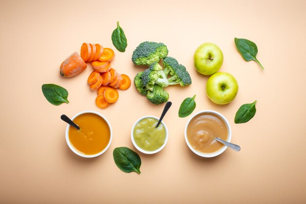 White bowls with healthy natural baby food on pastel background. Purees, made of fresh organic fruit and vegetables, flay lay, top view, concept. Kids food made from carrot, broccoli, apples, spinach