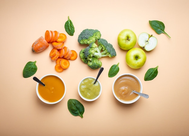 White bowls with healthy natural baby food on pastel background. Purees, made of fresh organic fruit and vegetables, flay lay, top view, concept. Kids food made from carrot, broccoli, apples, spinach