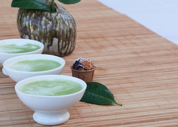 белые миски с зеленым чаем маття-латте на бамбуковом коврике, небольшой кусочек кекса