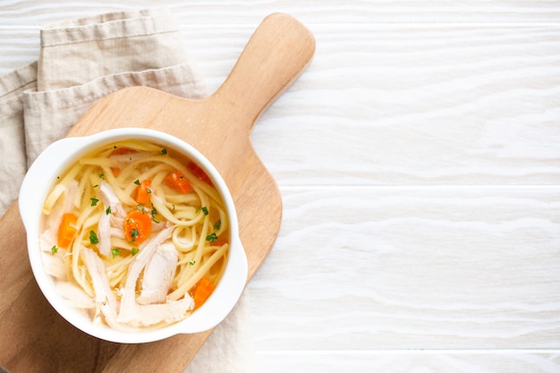 White bowls with warm healthy homemade chicken soup for dinner, white wooden table background. Traditional tasty chicken soup great for health and immune system. Top view, space for text