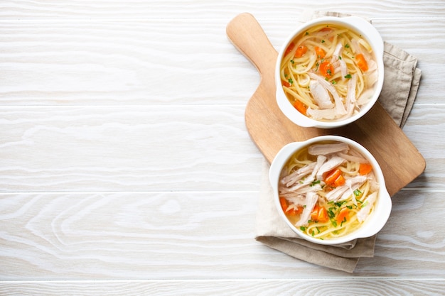 Photo white bowls with warm healthy homemade chicken soup for dinner, white wooden table background. traditional tasty chicken soup great for health and immune system. top view, space for text