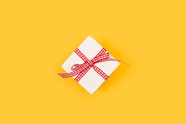 A white box with a red and white chequered bow on a yellow background with copy space