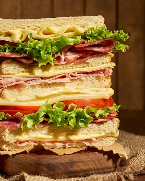 сэндвич из белого хлеба с ветчиной, салатом, сыром и помидорами, вид спереди