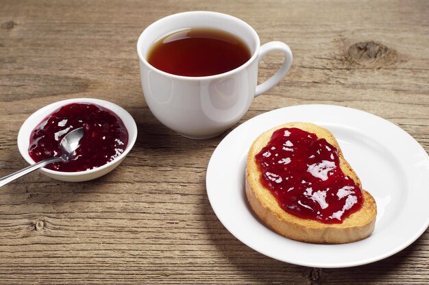 White bread with jam and tea cup on rustic wooden table