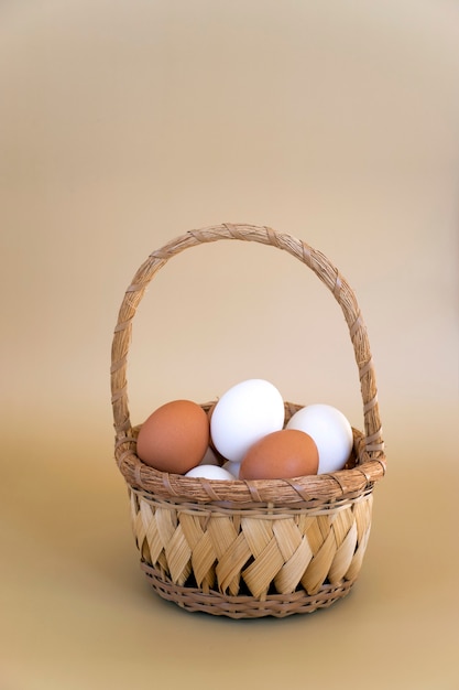 Photo white and brown eggs in wicker basket on pastel beige background. fresh chicken eggs, easter composition.