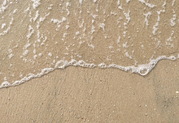 Белый пузырь морской волны на мелком песке на пляже