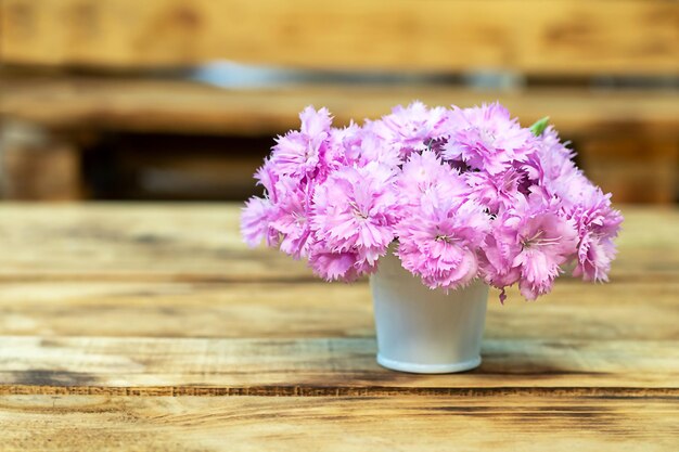 木製のテーブルにパステルピンクのカーネーションの花と白いバケツ