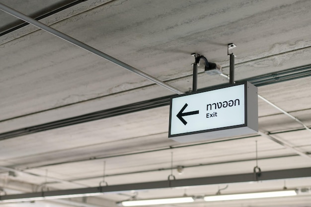 Photo a white building exit sign hung from the ceiling under the lights