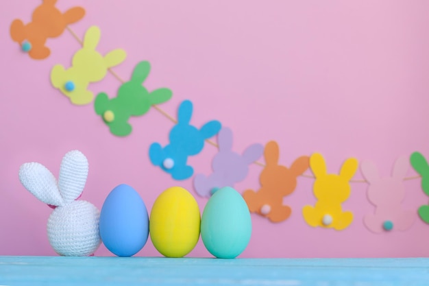 White bunny toy with colorful eggs and decoration on pink Easter background copy space