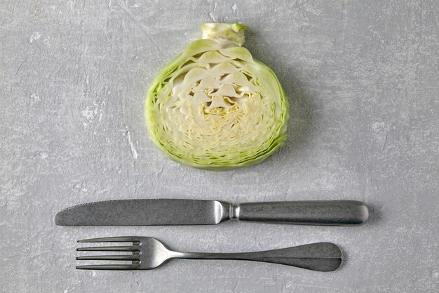 White cabbage in cross section and fork and knife on a gray concrete countertop