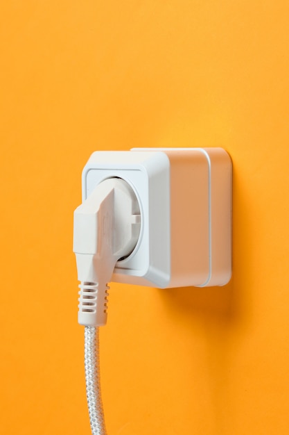 White cable plugged into power outlet on orange wall