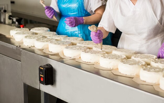 Белые пирожные на конвейере Рабочие вручную украшают торт Напряженный день на кондитерской фабрике Искусство может быть вкусным