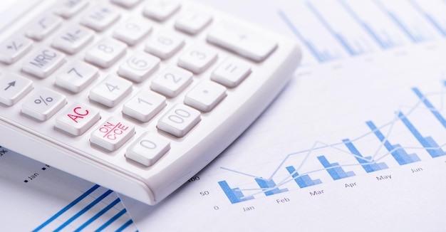 White calculator and report with chart and graph concept of annual financial profit overview banking and investment close up copy space macro