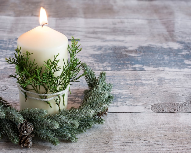 White candle burning on wooden ground with fir tree branch