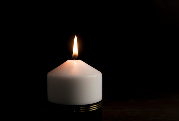 White candle with black ribbon, symbol of remembrance or\
mourning, black background. copy space.