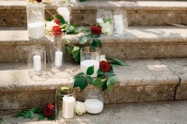 Candele bianche in barattoli di vetro circondate da rose stanno su gradini di pietra