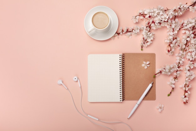 Una tazza da cappuccino bianca con fiori di sakura, notebook, cuffie, penna