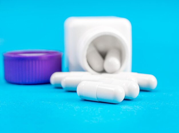 White capsules with white container and his cap on blue background Close up